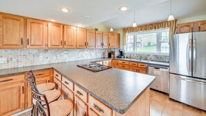 A kitchen with wooden cabinets, granite countertops, stainless steel appliances, and a large island with bar stools. - Scenic Views: Spacious Webster Lake House! (North Webster)