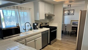 A compact kitchen with a microwave, sink, stove, and dishwasher. There is a dining area with a table and chairs visible in the background. - 4BR/2.5BA House in Delightful Lancaster with WiFi, AC and Large Yard (Lancaster)