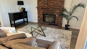 A living room with a brick fireplace, a glass coffee table, and a sofa. - 4BR/2.5BA House in Delightful Lancaster with WiFi, AC and Large Yard (Lancaster)