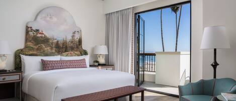 A hotel room with a large bed, a bench, a chair, a painting, a nightstand, a lamp, and a view of the outdoors.