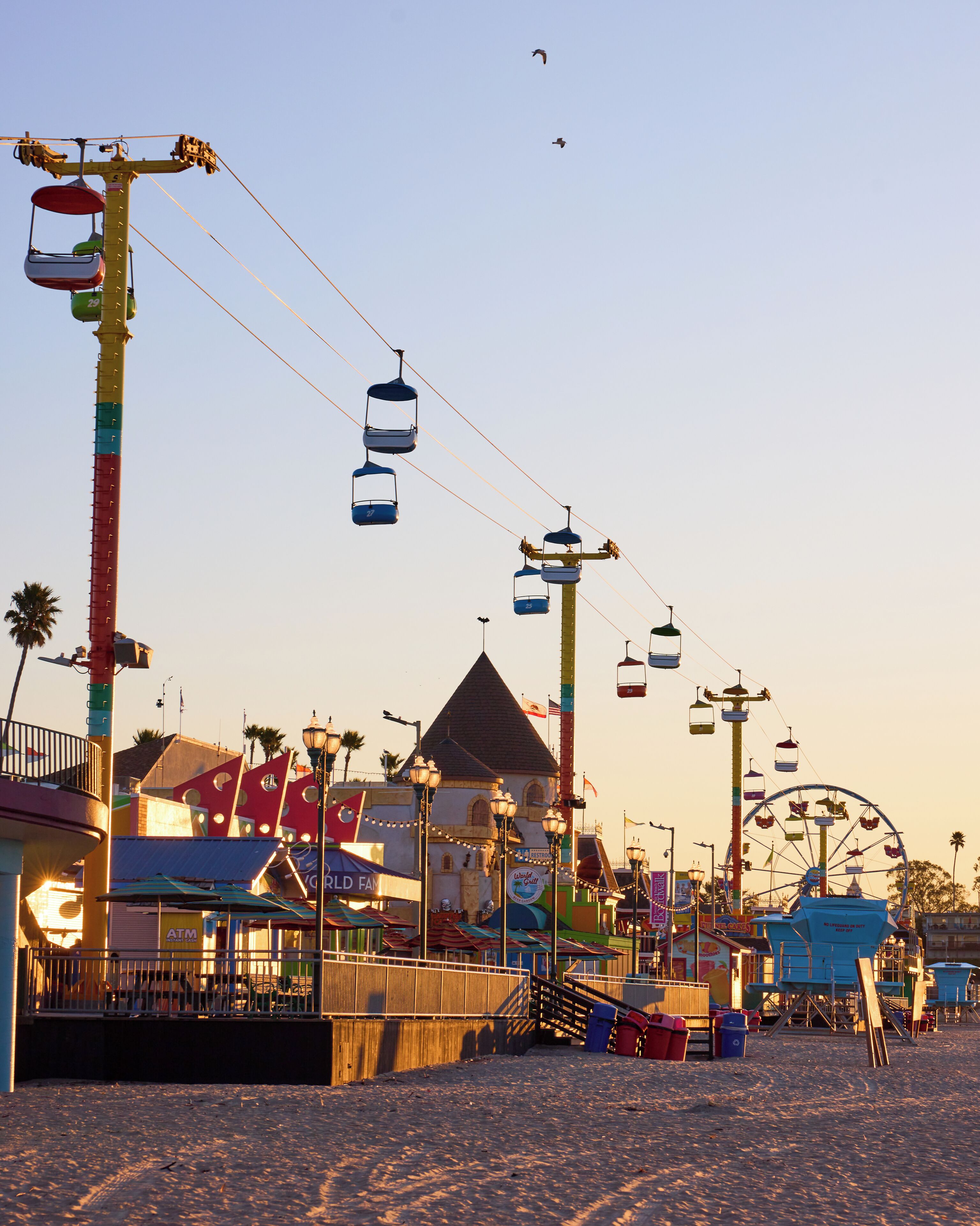 A beachside amusement park with a Ferris wheel, a roller coaster, and a cable car system.