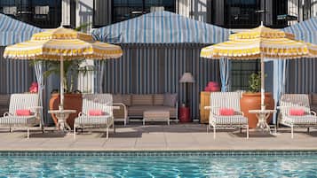 Een zwembadgedeelte met gestreepte parasols, ligbedden en een loungebank.