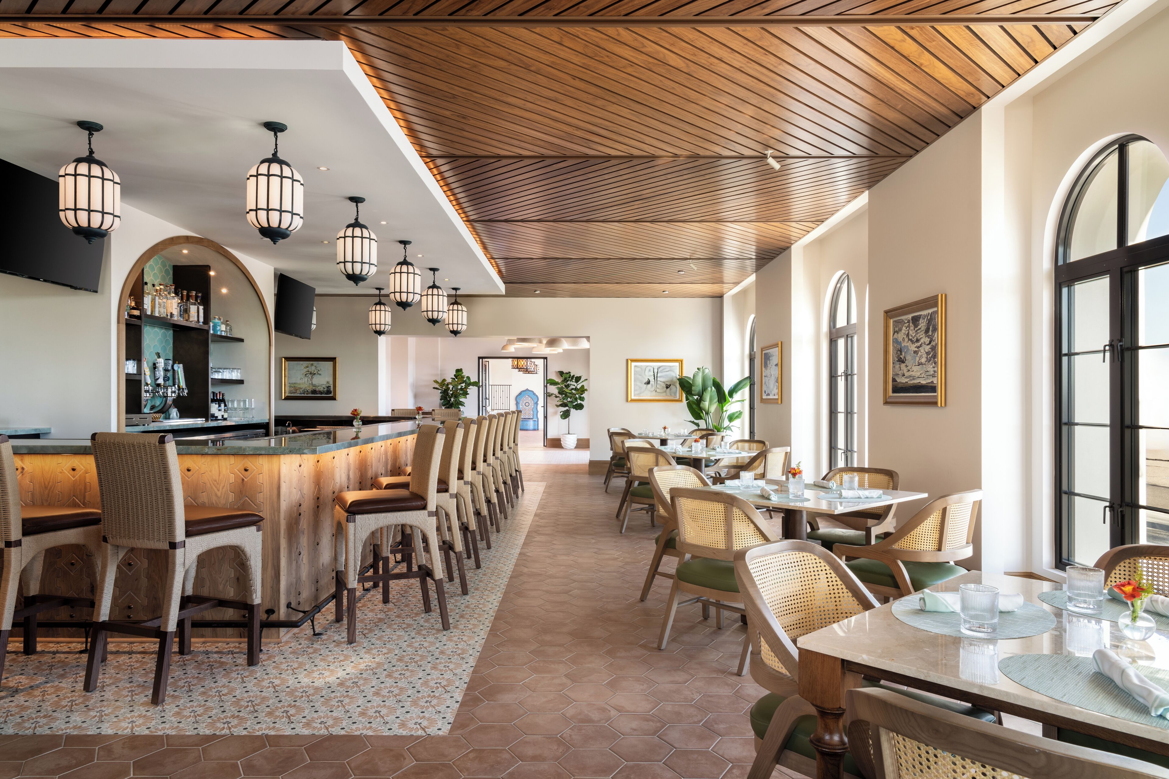 Un restaurante con zona de bar, techo de madera y ventanas amplias.