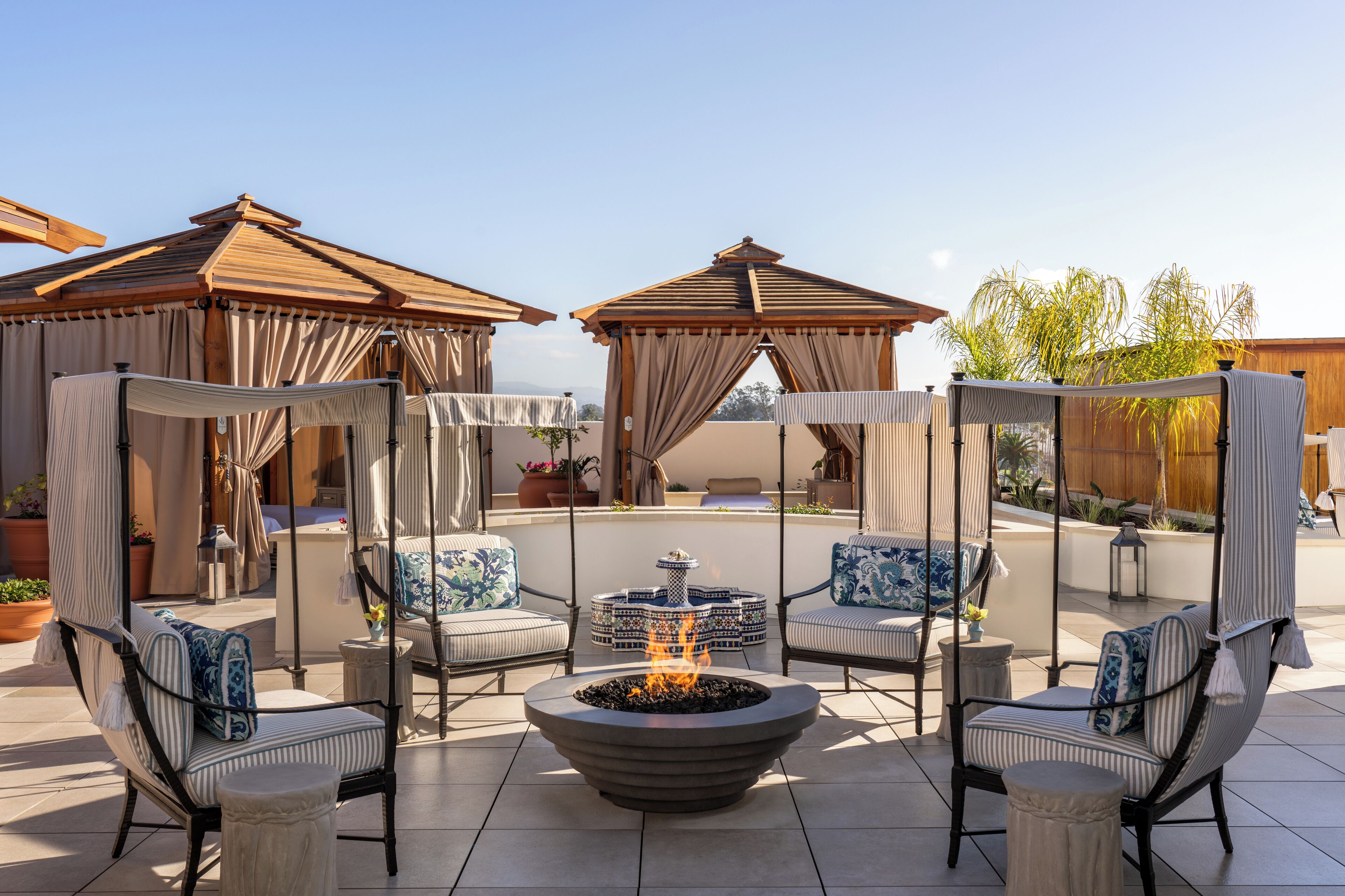 A patio area with a fire pit, cushioned seating, and covered gazebos.