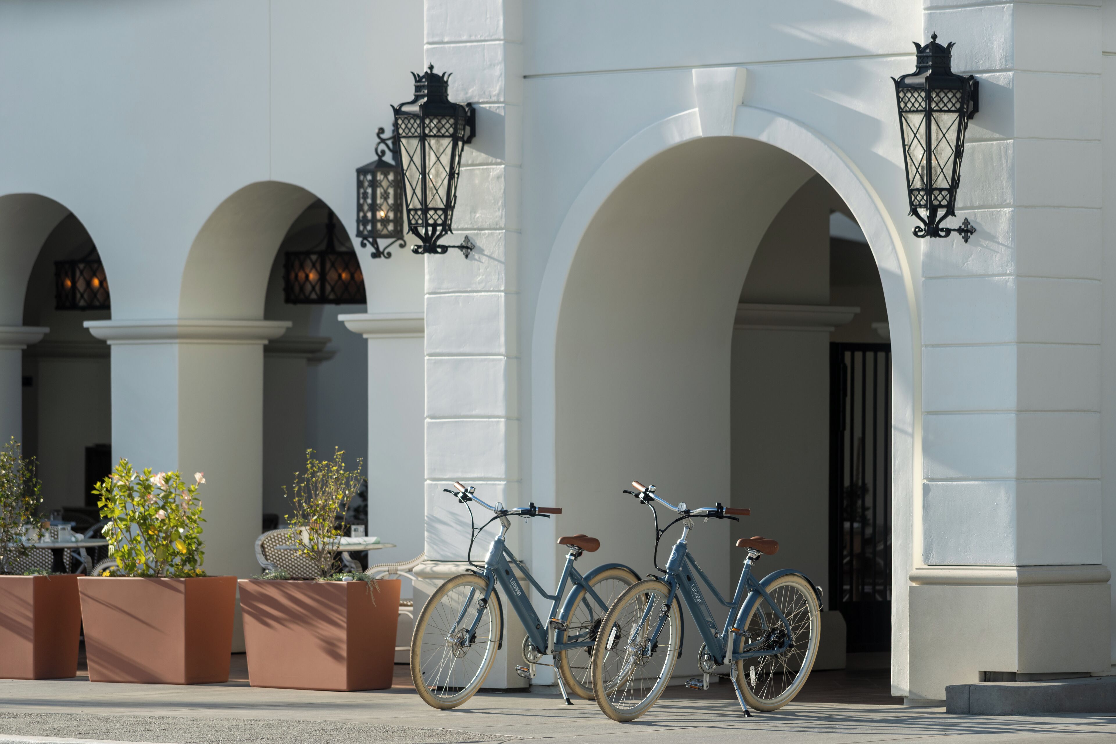 A building with white columns and arches, two bicycles parked in front, and potted plants.
