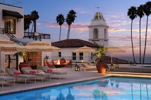 A poolside area with lounge chairs, umbrellas, and a building with a bell tower. - La Bahia Hotel and Spa (Santa Cruz)
