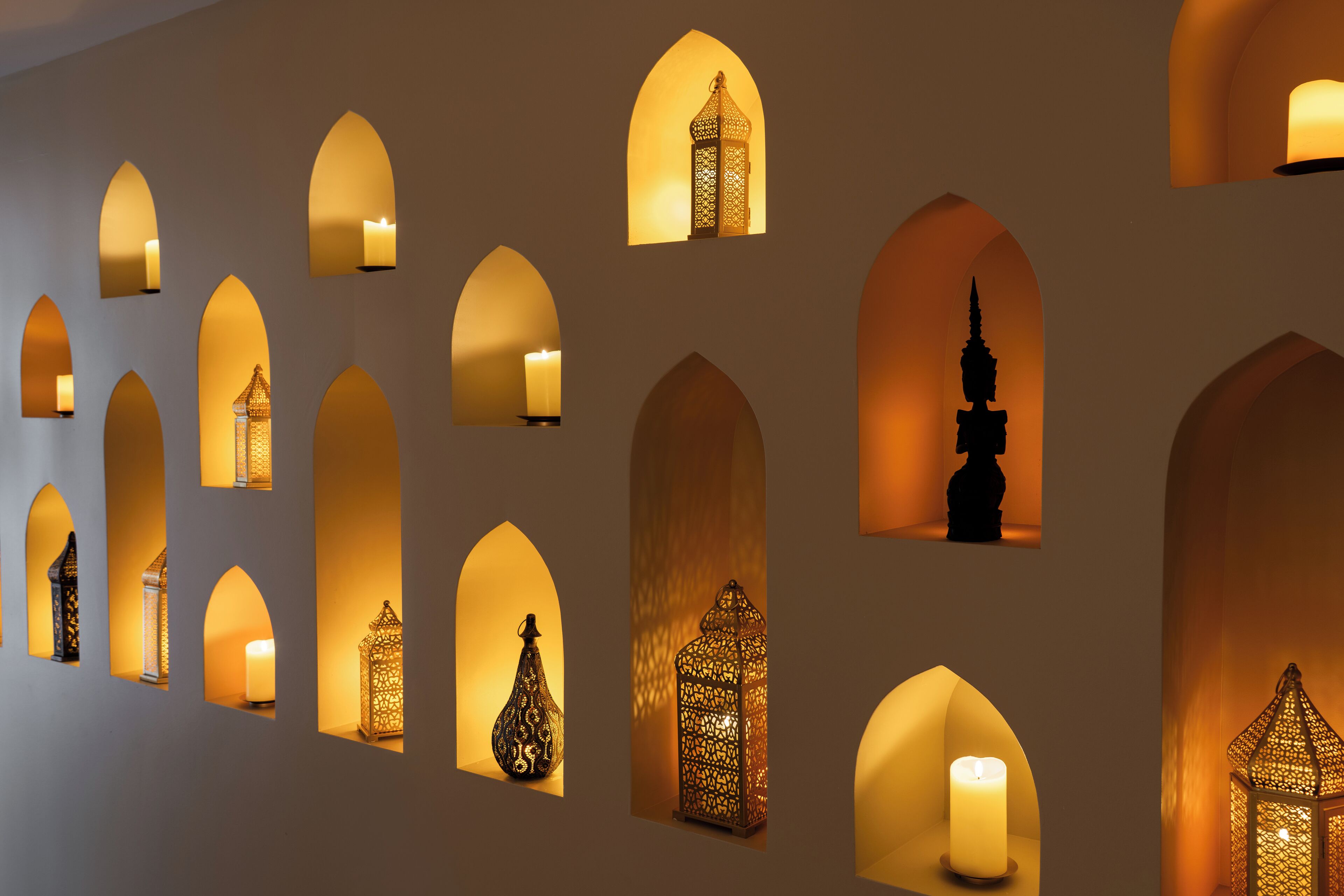 A wall with multiple arched openings, each containing a candle or a lantern.