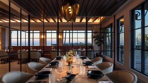 Comedor con una larga mesa dispuesta para una comida, ventanas amplias que ofrecen vistas y un diseño moderno en el techo.