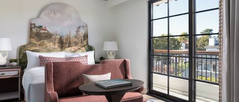 A hotel room with a bed, a sofa, a small table, and a large window with a view of the outside.