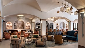 Un hallo espacioso con techos altos, ventanas de arco y diversas opciones de asientos, incluyendo sofás, sillones y una zona de bar.