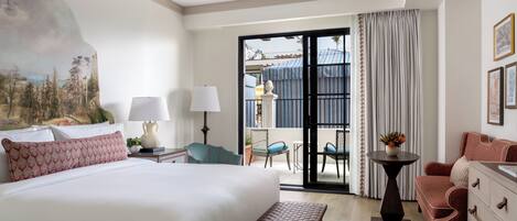 A hotel room with a large bed, a bench, a desk, a chair, a dresser, and a view of the outside balcony.