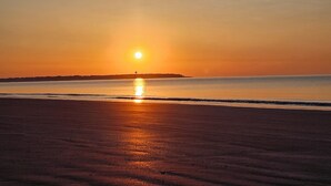 Un atardecer sobre una playa con aguas tranquilas que reflejan el sol.