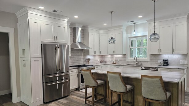 Una cocina moderna con armarios blancos, electrodomésticos de acero inoxidable y una isla central con taburetes de bar.