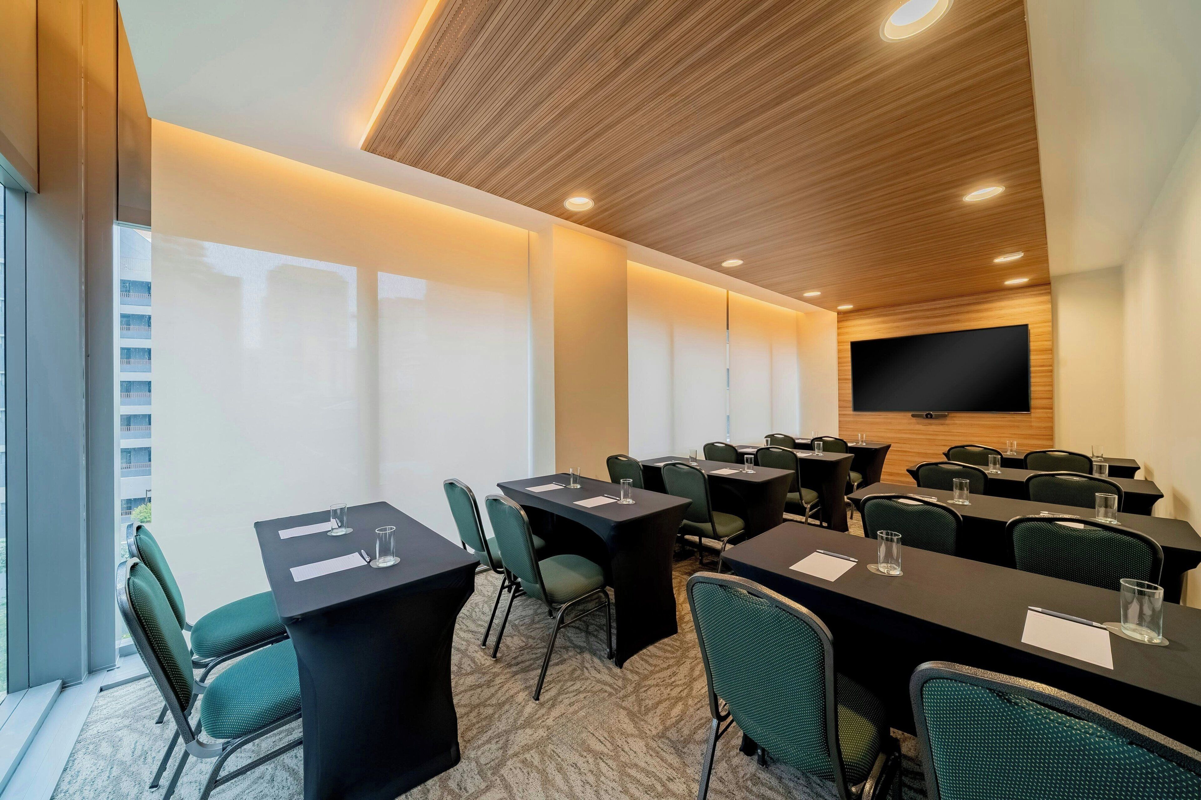 A conference room with tables and chairs, a large screen, and a view of a building outside.