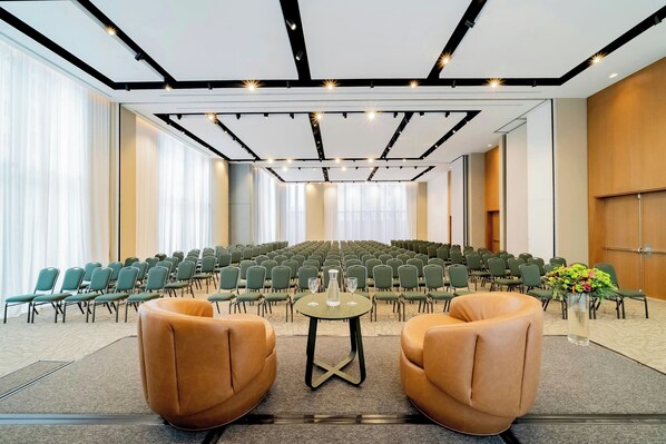 A conference room with rows of chairs, a stage, and two leather armchairs.