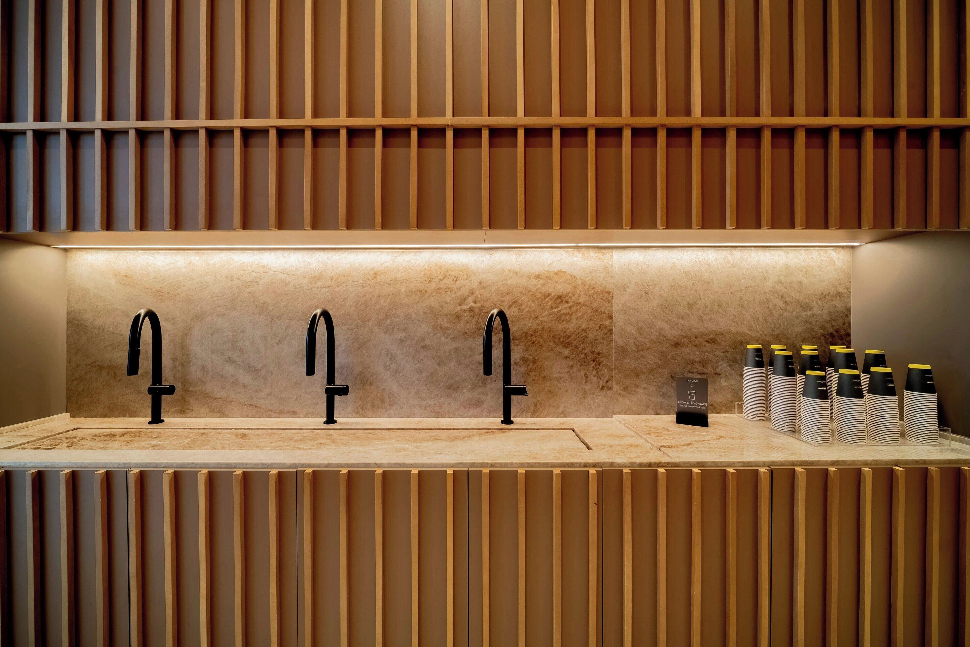 A modern bathroom with three black faucets and a row of stacked toiletries.