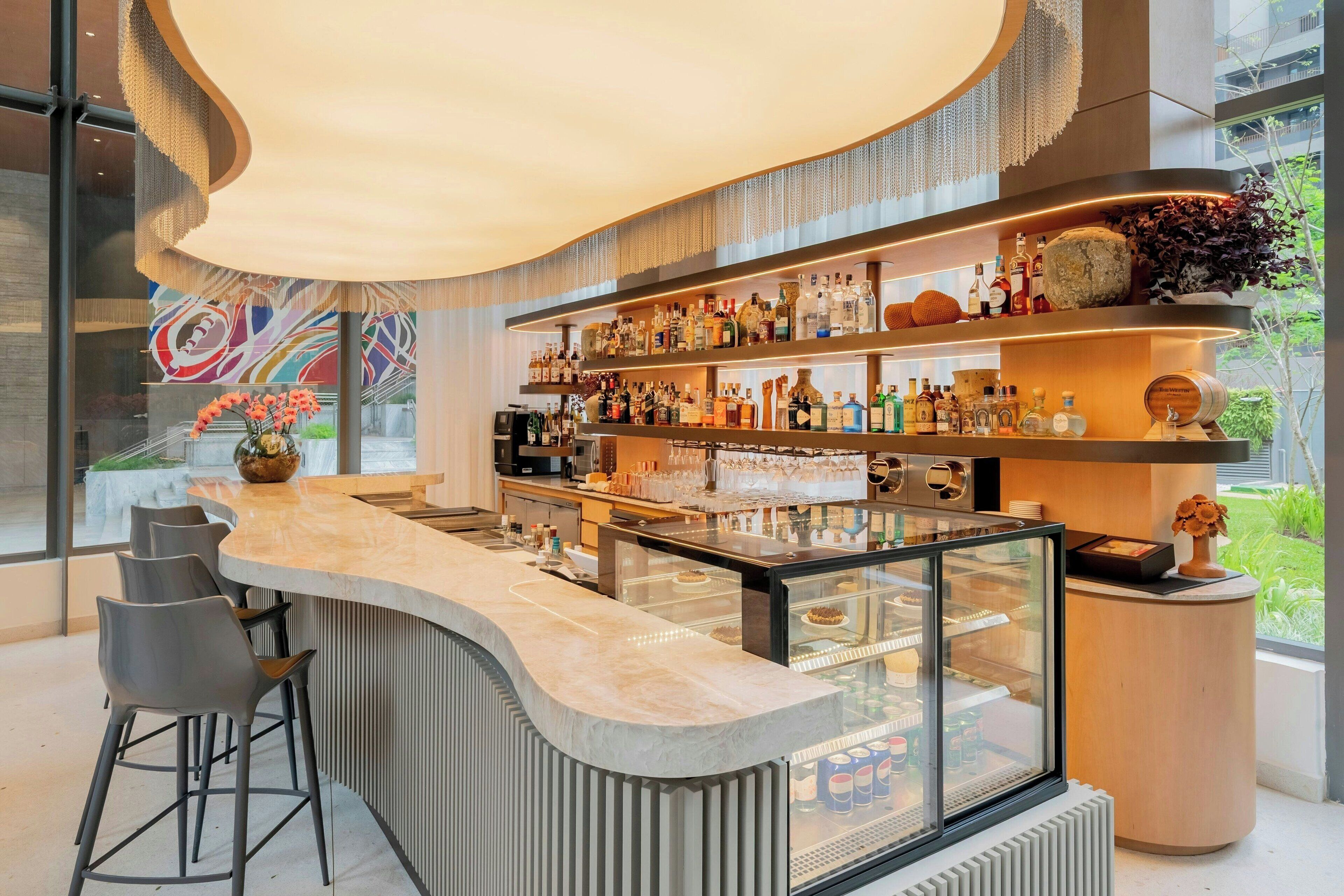Uma área de bar moderna com um balcão curvo, banquetas e uma vitrine de vidro.