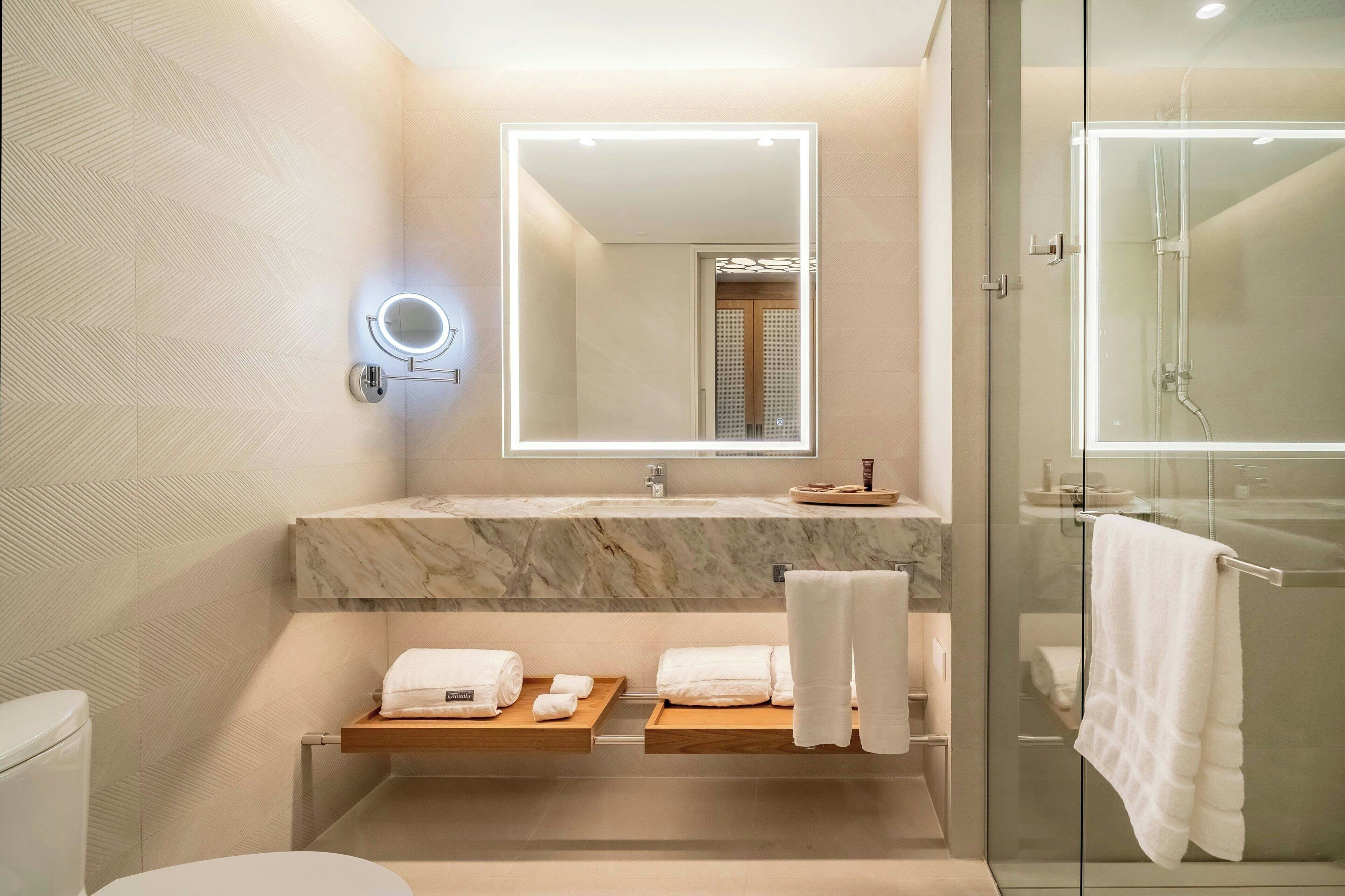 Un bagno moderno con un vanità in marmo, una cabina doccia in vetro e uno specchio con illuminazione integrata.