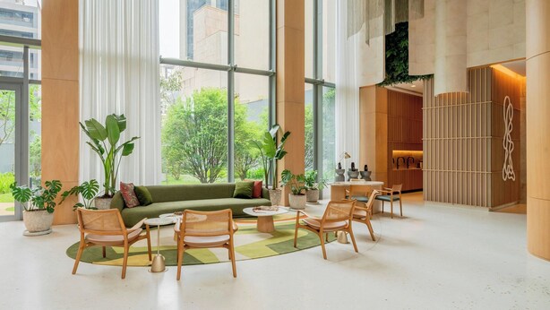 Un'ampia hall con ampie finestre, un divano verde, poltrone in vimini e piante in vaso.