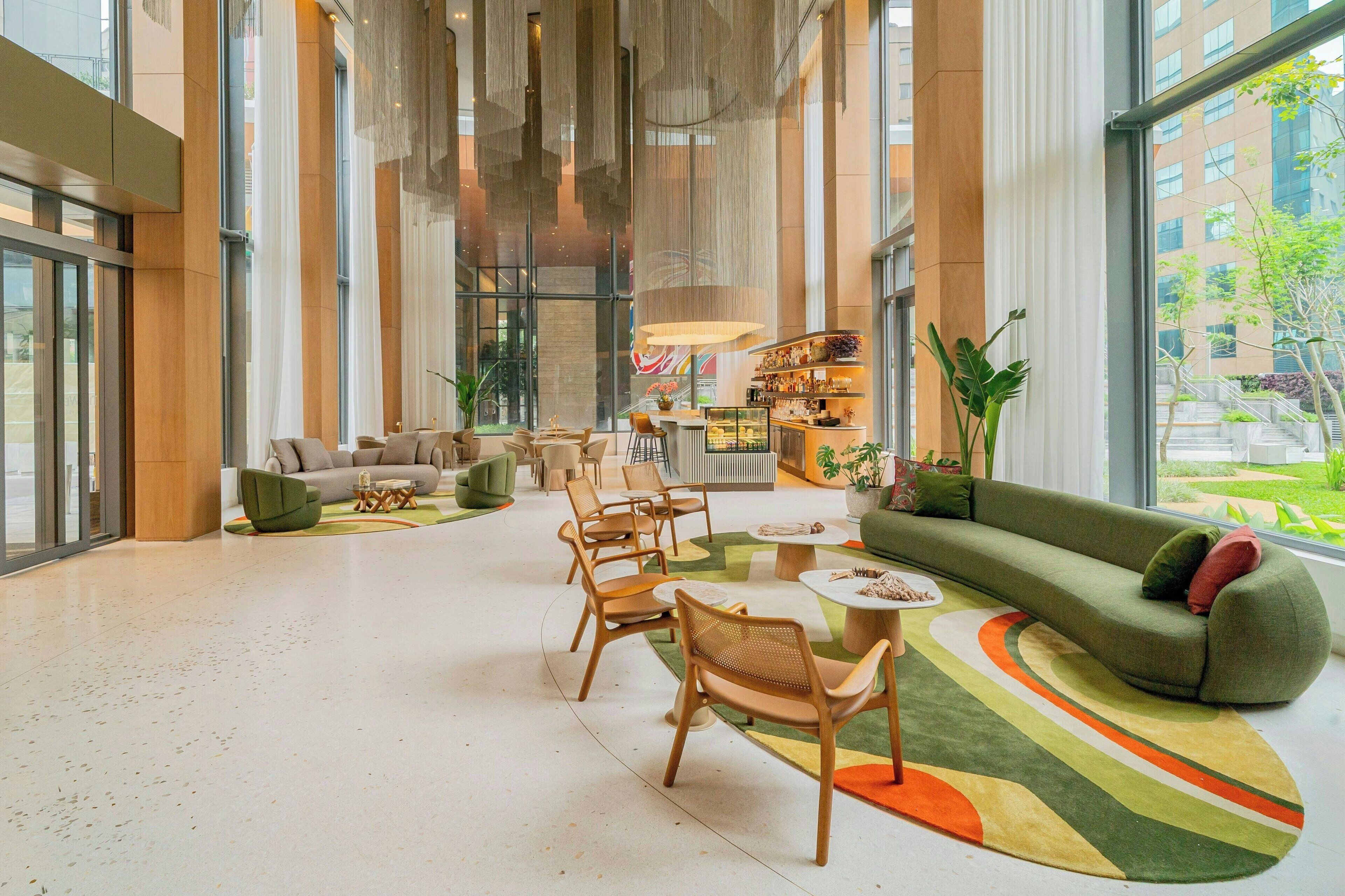 A spacious lobby with a green sofa, wooden chairs, a coffee table, and a large window offering a view of the outdoors.