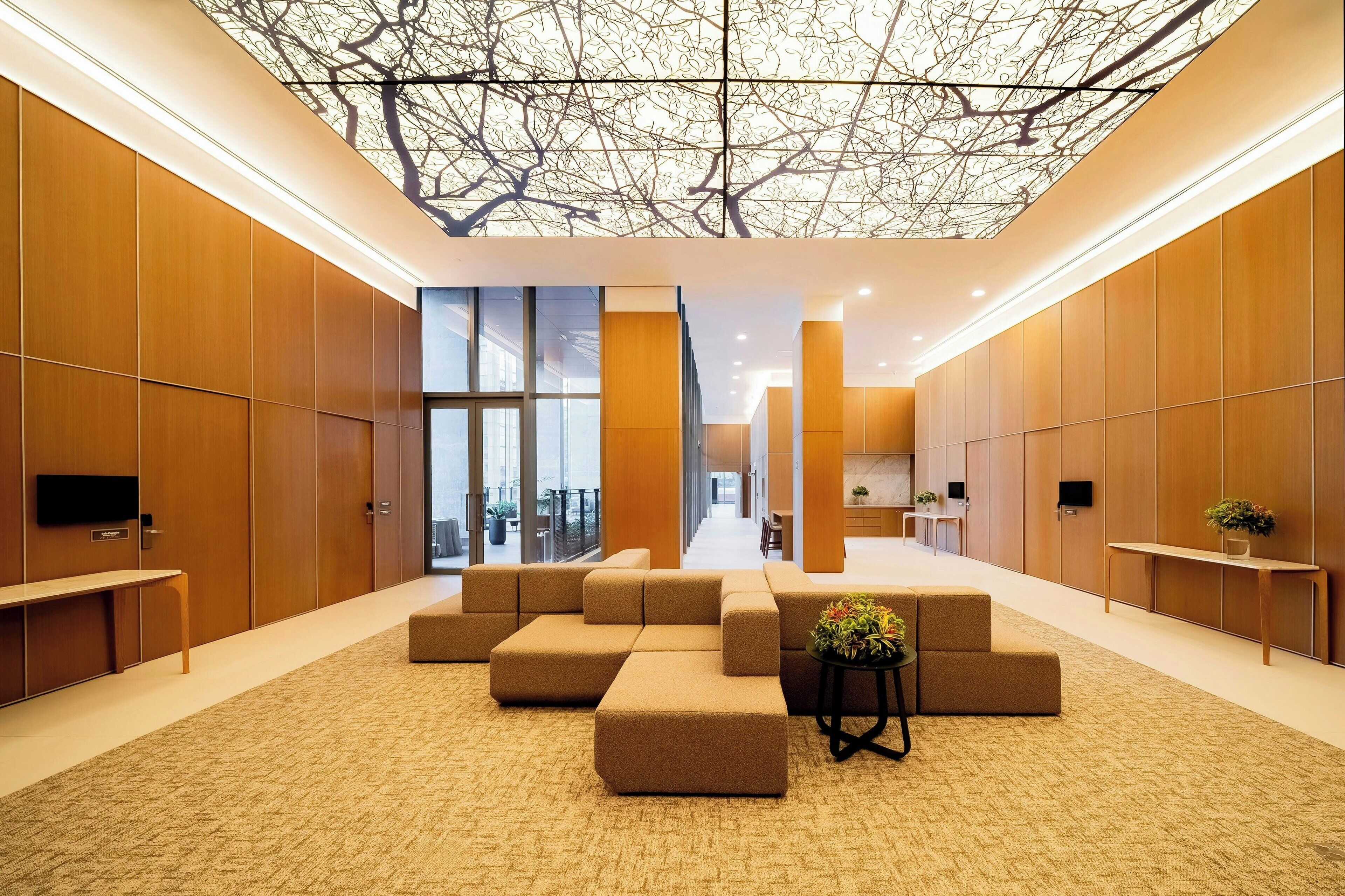 A modern lobby with a high ceiling, wooden panel walls, and a central seating area with sofas and a small table.
