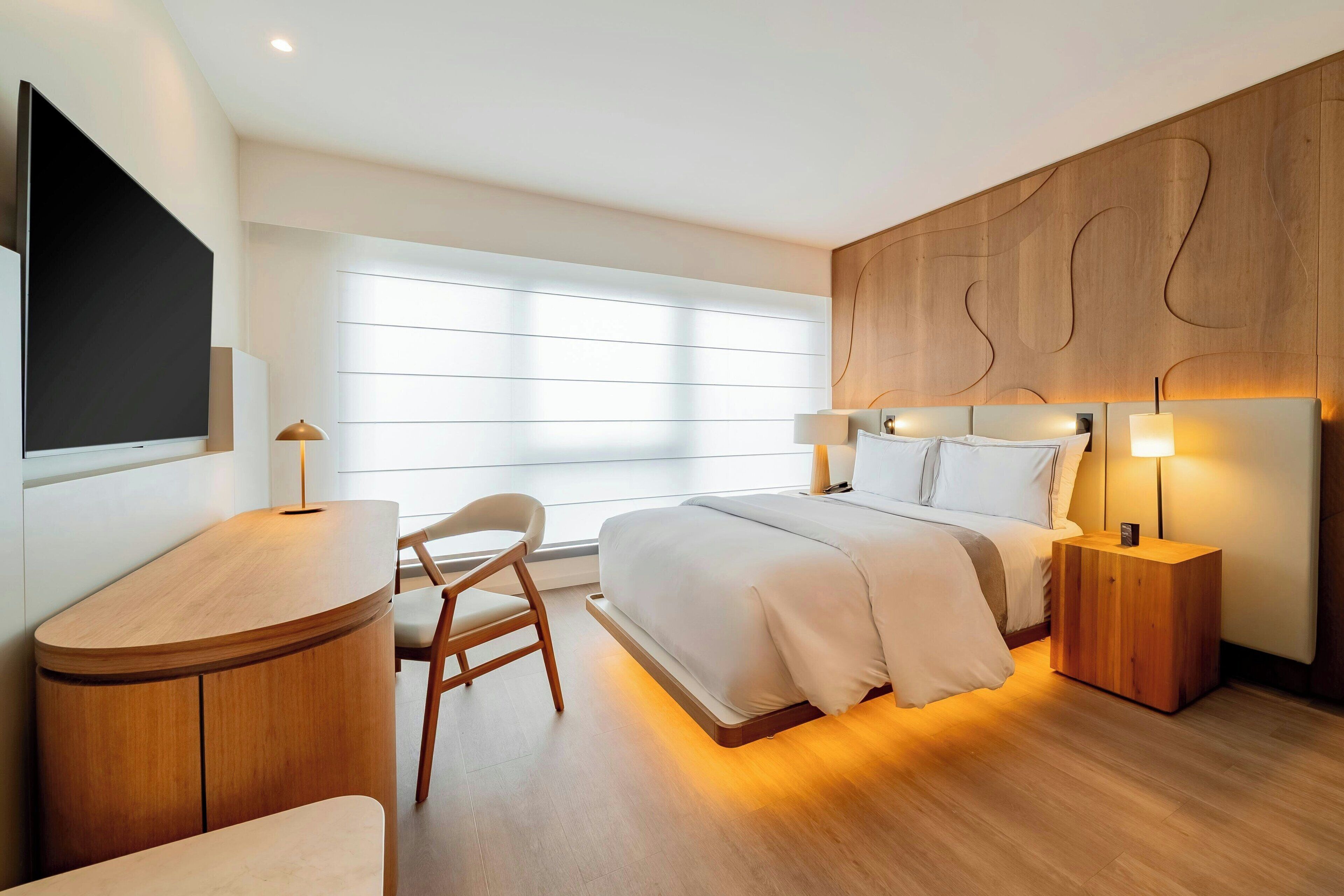Un dormitorio moderno con una cama, mesitas de noche, un escritorio y una silla.