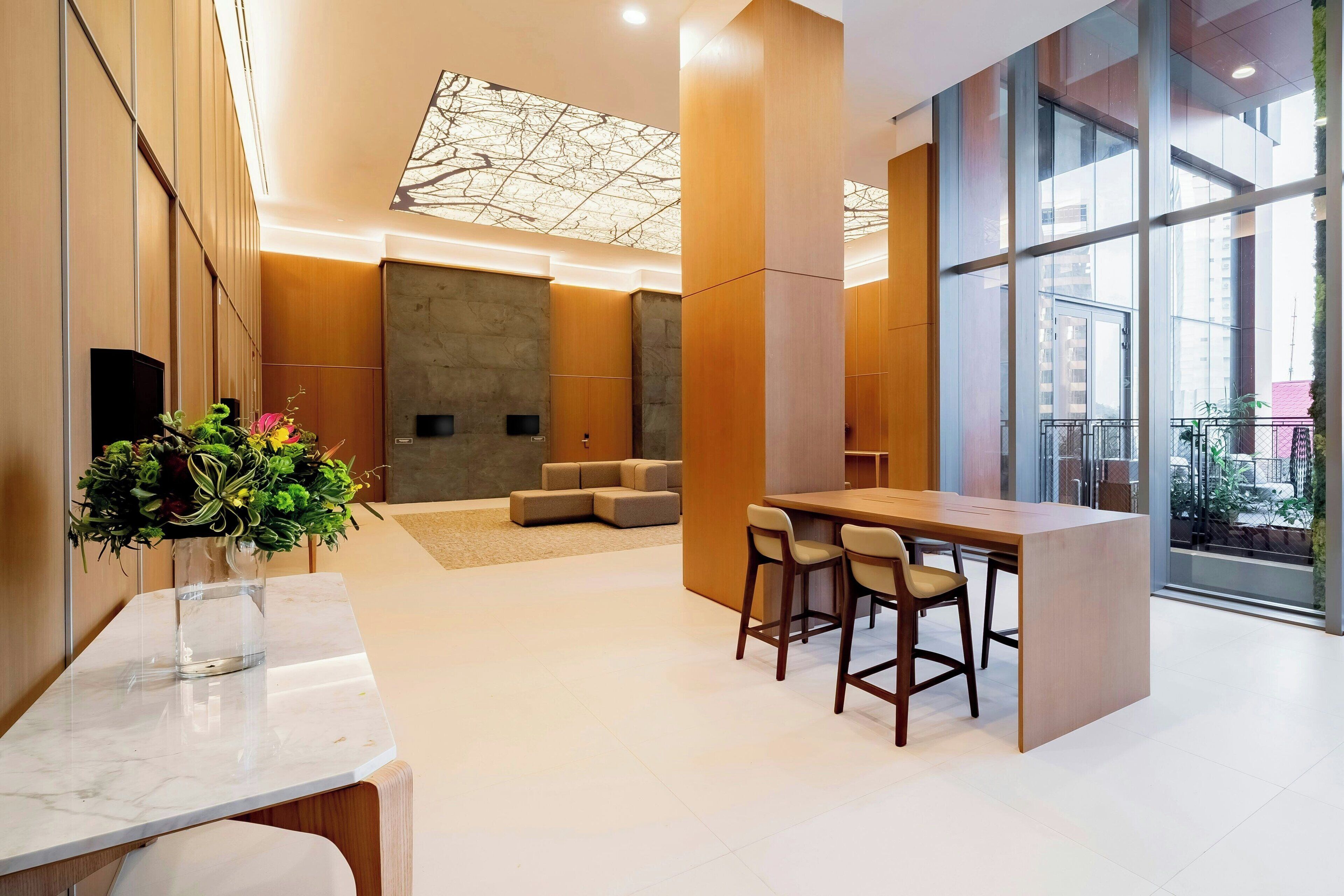 A modern lobby with a marble reception desk, a seating area with sofas, and large windows offering a view of the city.