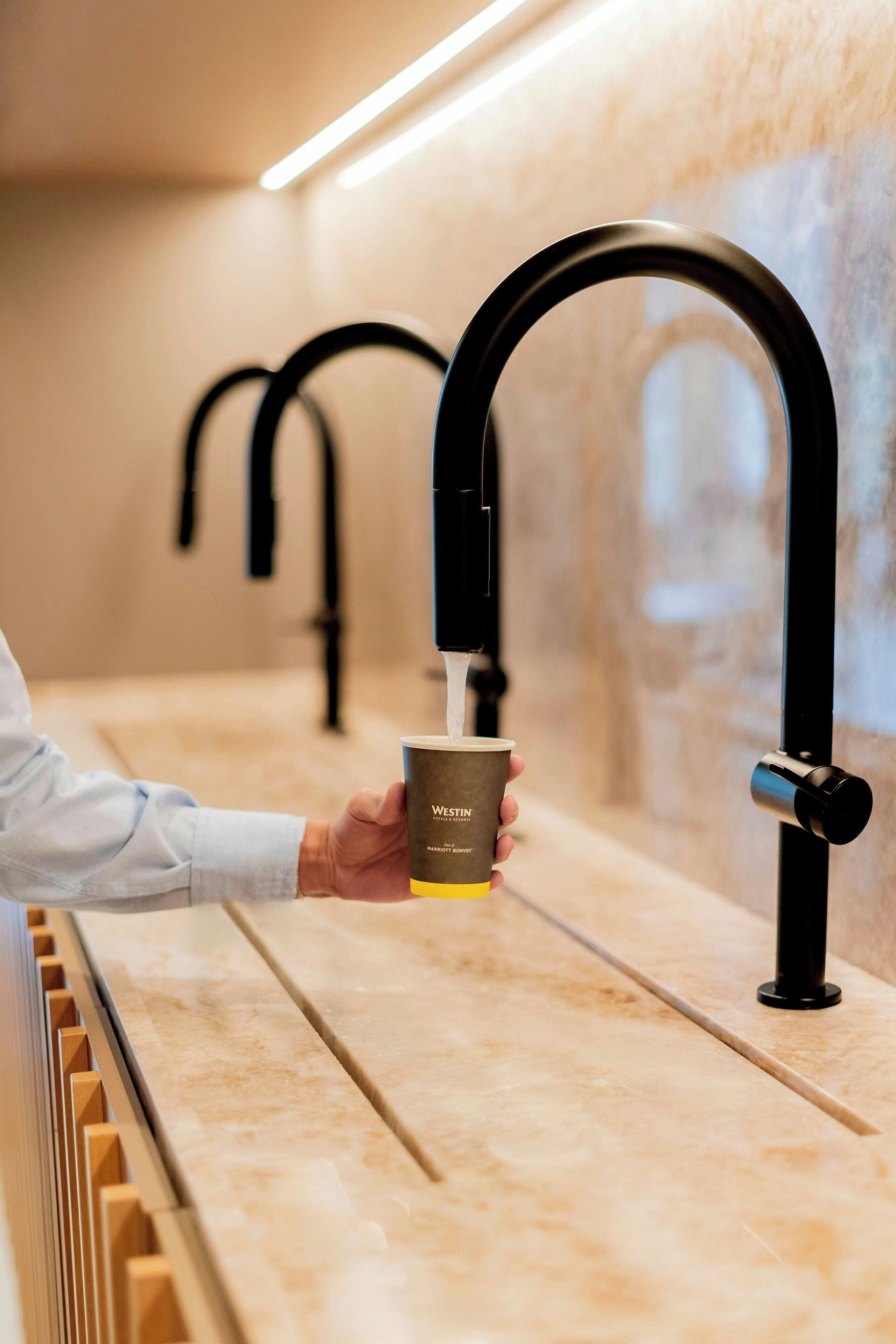 Une personne tenant une tasse de café devant une machine à café moderne et élégante, au design minimaliste.