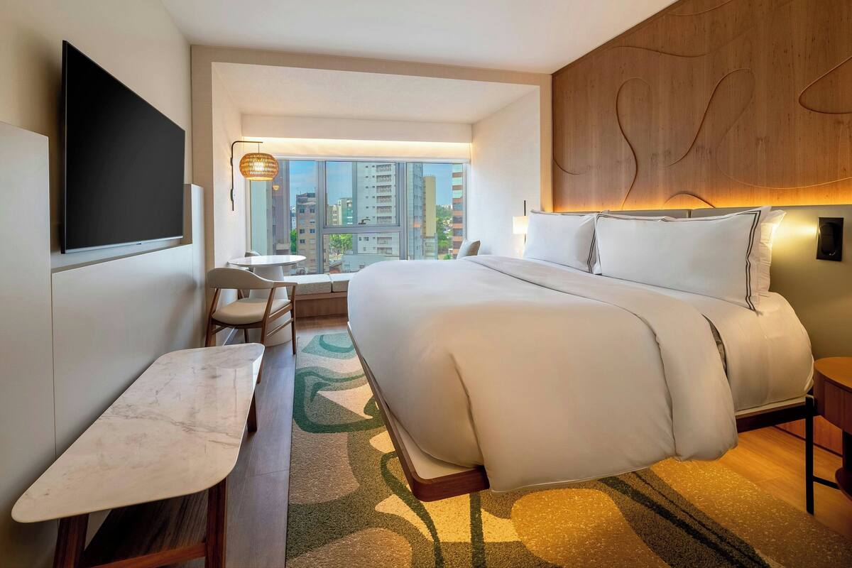 Ein Hotelzimmer mit einem großen Bett, einem Schreibtisch, einem Flachbildfernseher und Blick auf die Stadtlandschaft.