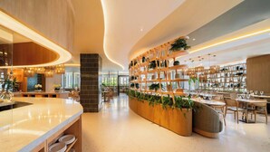 Un interno moderno con una reception dalla forma sinuosa, scaffali in legno con piante e un’area salotto con tavoli e sedie.
