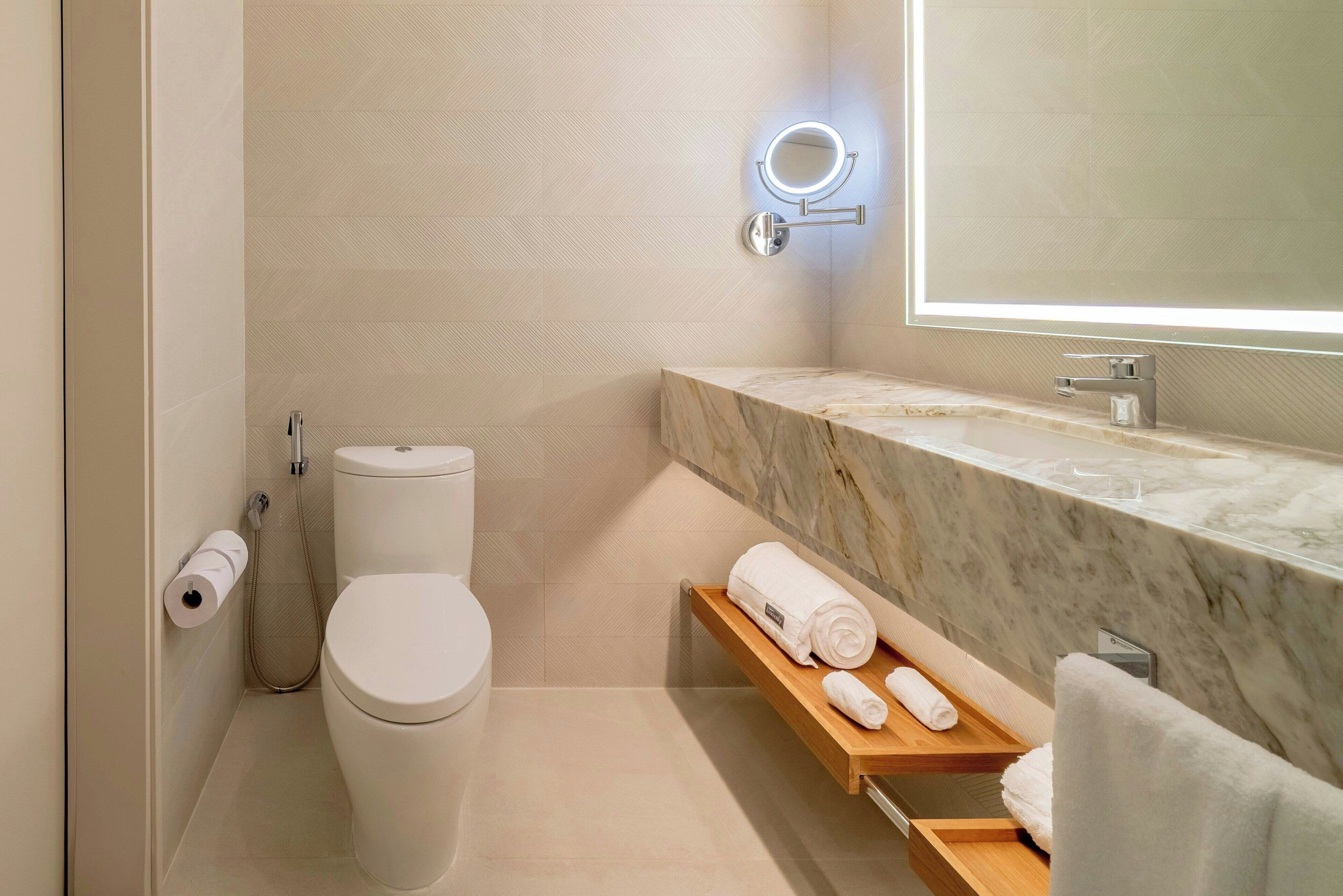 Un baño moderno con inodoro, lavamanos de mármol, espejo con luz y toallero.