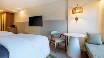 A hotel room with two beds, a TV mounted on the wall, a small round table, a chair, and a sofa.