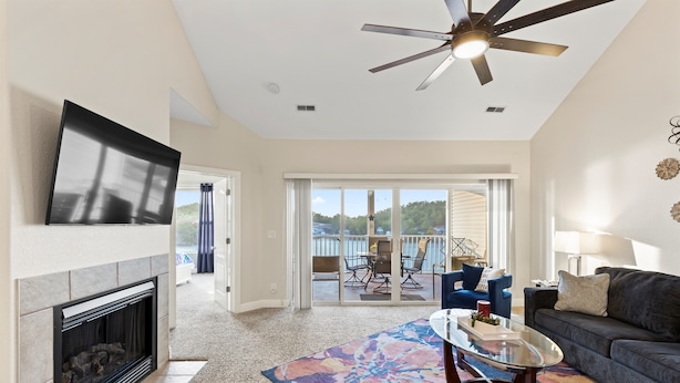 A spacious living room with a fireplace, a ceiling fan, a large TV, and a balcony with outdoor furniture.