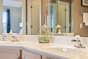 A bathroom with a white sink, two gold geometric glass vases with plants, a mirror, and a white towel hanging on the wall.