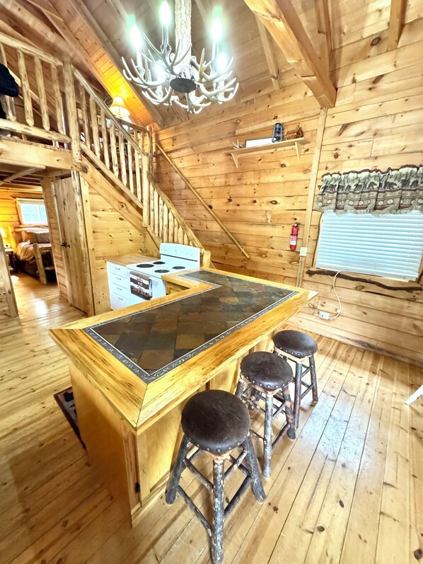 A wooden cabin interior with a central island bar, wooden floors, a staircase, and a chandelier.
