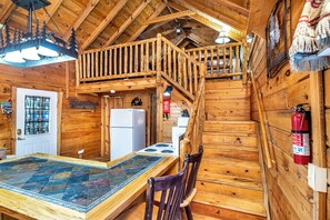 A wooden cabin interior with a dining table, chairs, a kitchen area, a staircase, and a ceiling light fixture. - Charming Log Cabin Fully Stocked 1.5 Garage Sleeps 7 UTV Route (Black River Falls)