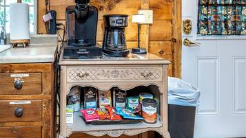 A kitchenette with a coffee maker, a kettle, and a coffee pot on a wooden countertop. Below, there are storage drawers labeled for wash rags and garbage bags.