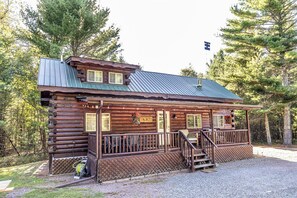 A log cabin with a porch, a covered front entrance, and a flagpole in the background.