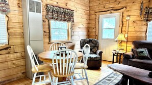 Ein gemütliches Blockhaus-Interieur mit einem Holztisch, weißen Stühlen, einem Ledersessel, einer Couch und einer Lampe.