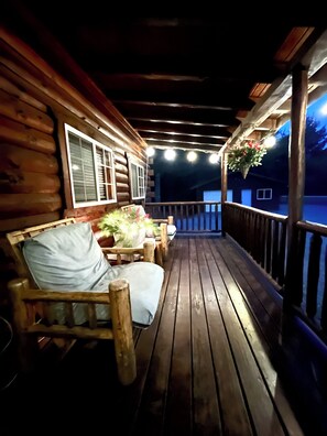 A wooden deck with a bench and potted plants, leading to a covered area with a railing. - Charming Log Cabin Fully Stocked 1.5 Garage Sleeps 7 UTV Route (Black River Falls)