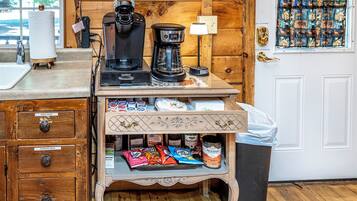 Een kitchenette met een koffiezetapparaat, een waterkoker en een koffiekan op het aanrecht. Er zijn kastjes met gelabelde lades voor washandjes en vuilniszakken.