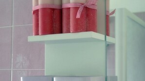 A bathroom with a white shelf holding several pink and white cylindrical containers, possibly toiletries, and a mirror with a blue frame. - Little house by the sea (Licinella-Torre di Paestum)