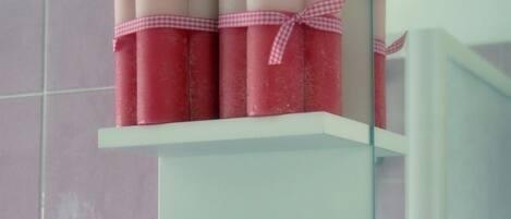 Un baño con un estante blanco que contiene varios recipientes cilíndricos rosa y blanco, posiblemente artículos de aseo, y un espejo con marco azul.