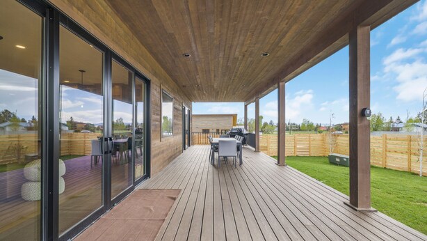Une terrasse extérieure couverte, dotée d’un plancher en bois, de murs en verre et d’une table avec des chaises.
