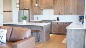 Une cuisine moderne avec des meubles en bois, un îlot central, des tabourets de bar et un réfrigérateur en acier inoxydable.