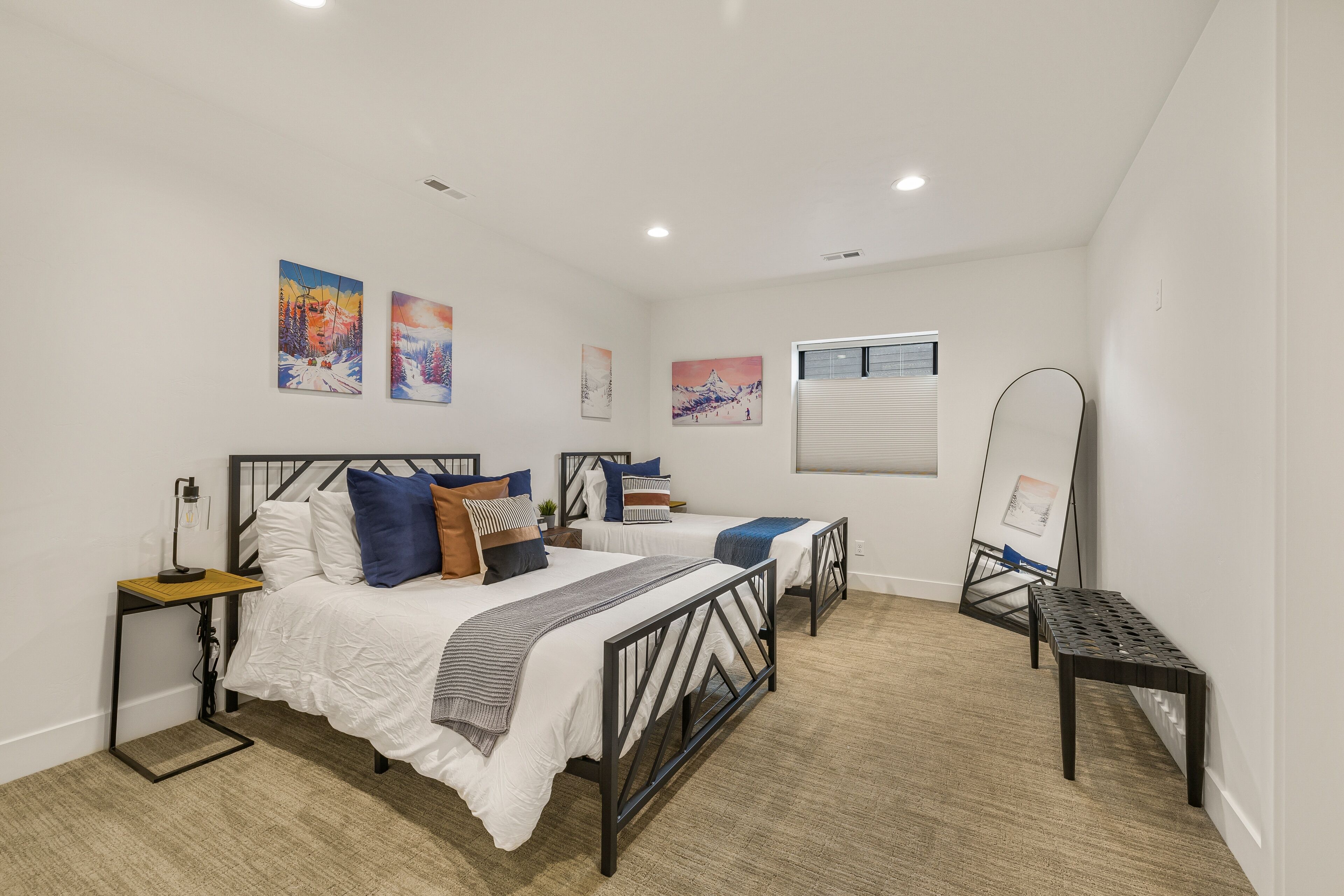 Quarto com duas camas, mesa de cabeceira, espelho e quadros nas paredes.