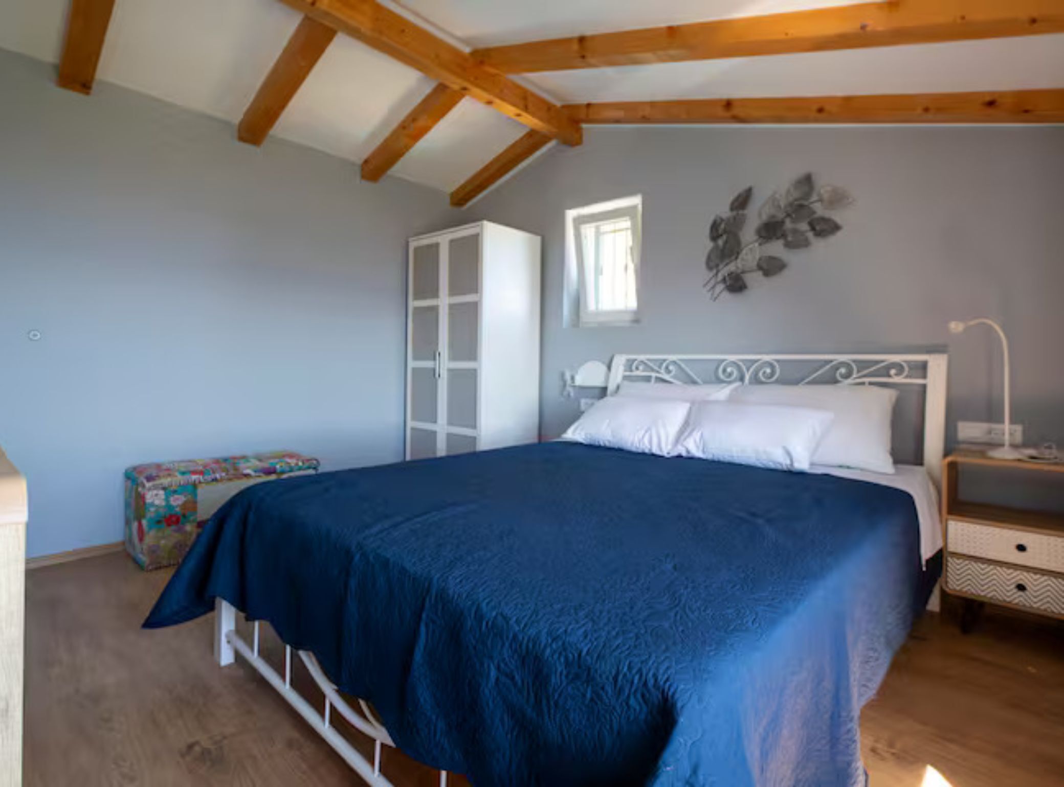 A bedroom with a bed, a wardrobe, a nightstand, and a window.