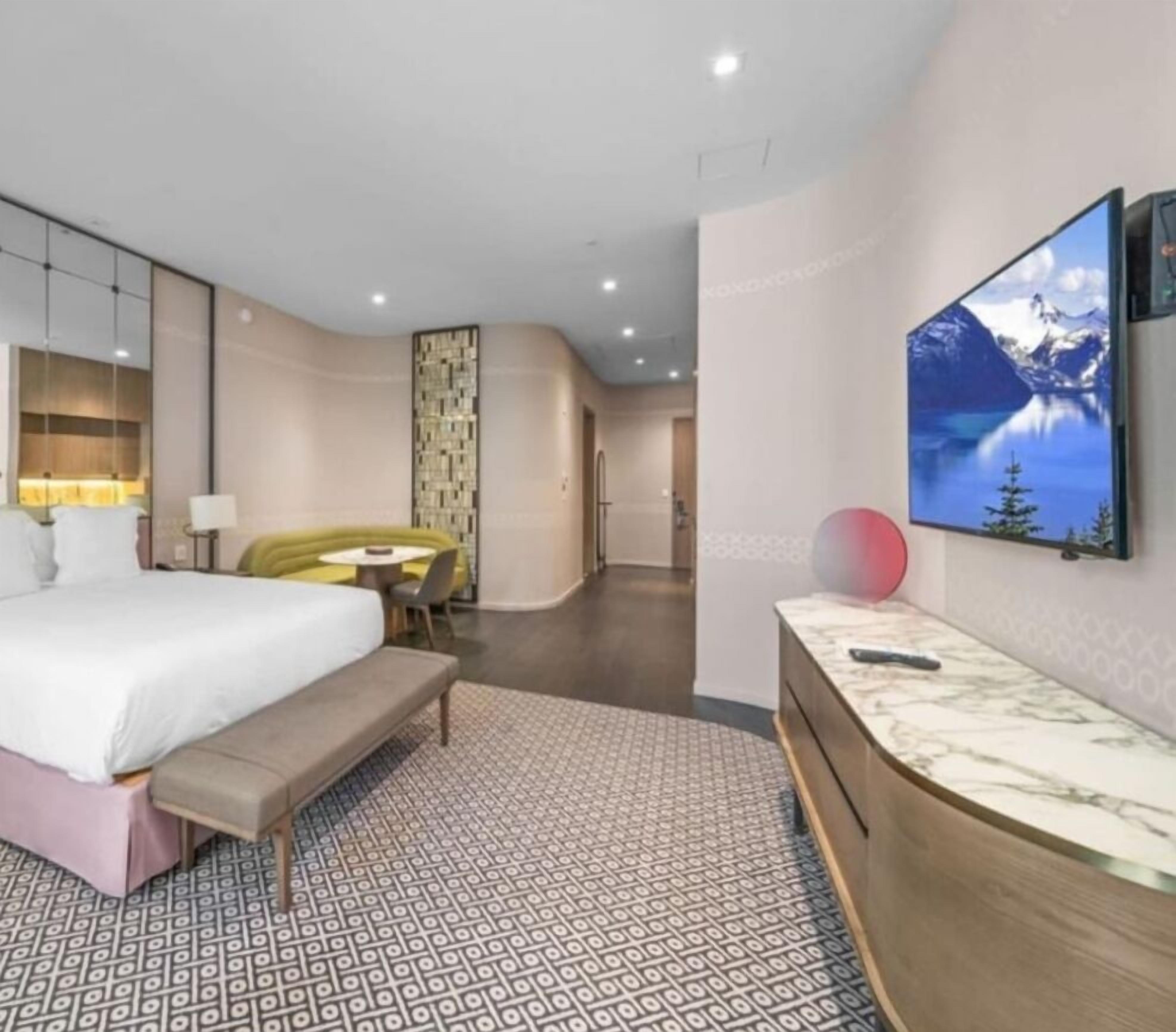 Ein modernes Hotelzimmer mit einem großen Bett, einem Schreibtisch und einem an der Wand montierten Fernseher.