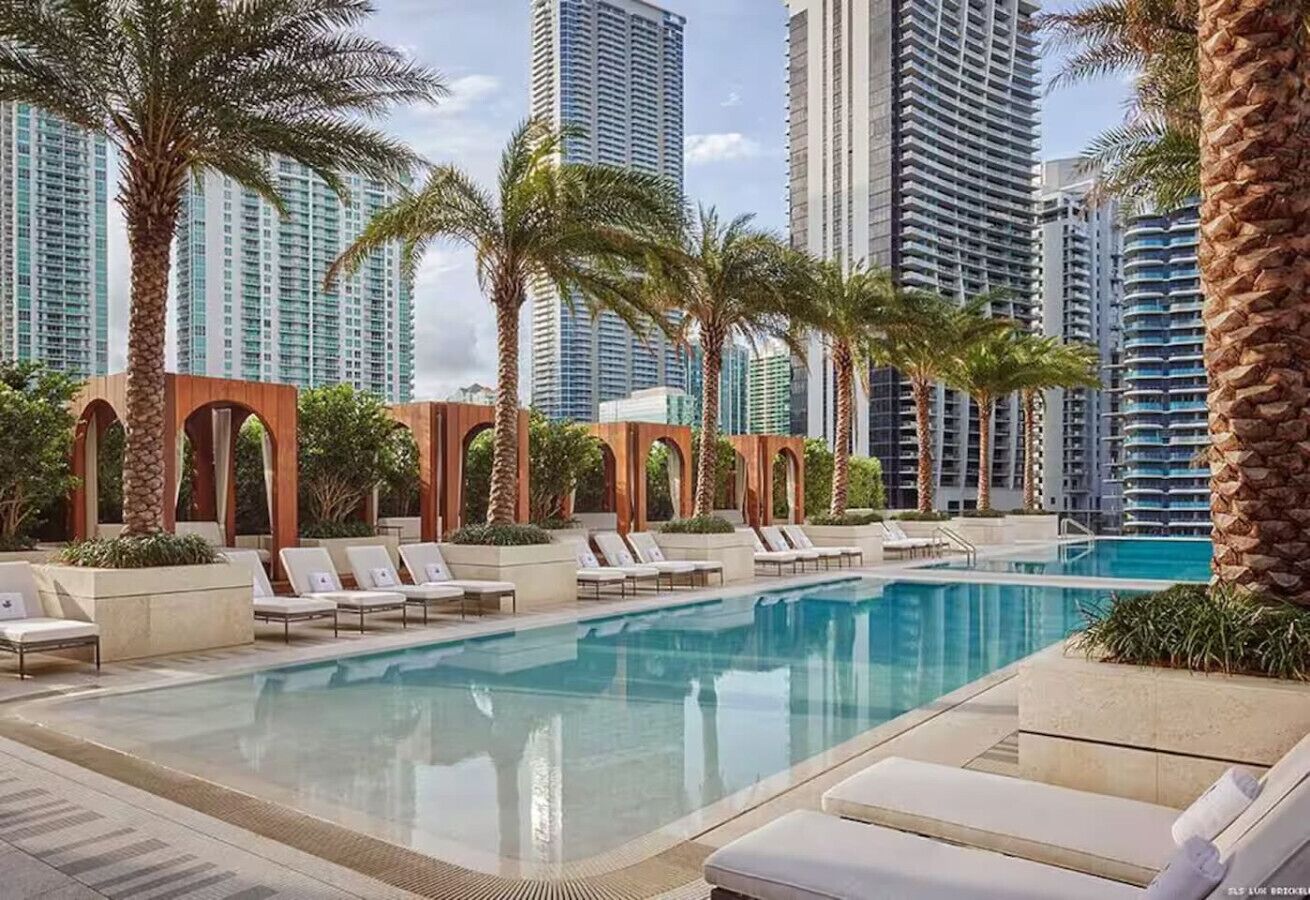 A pool area with lounge chairs and palm trees, surrounded by high-rise buildings.