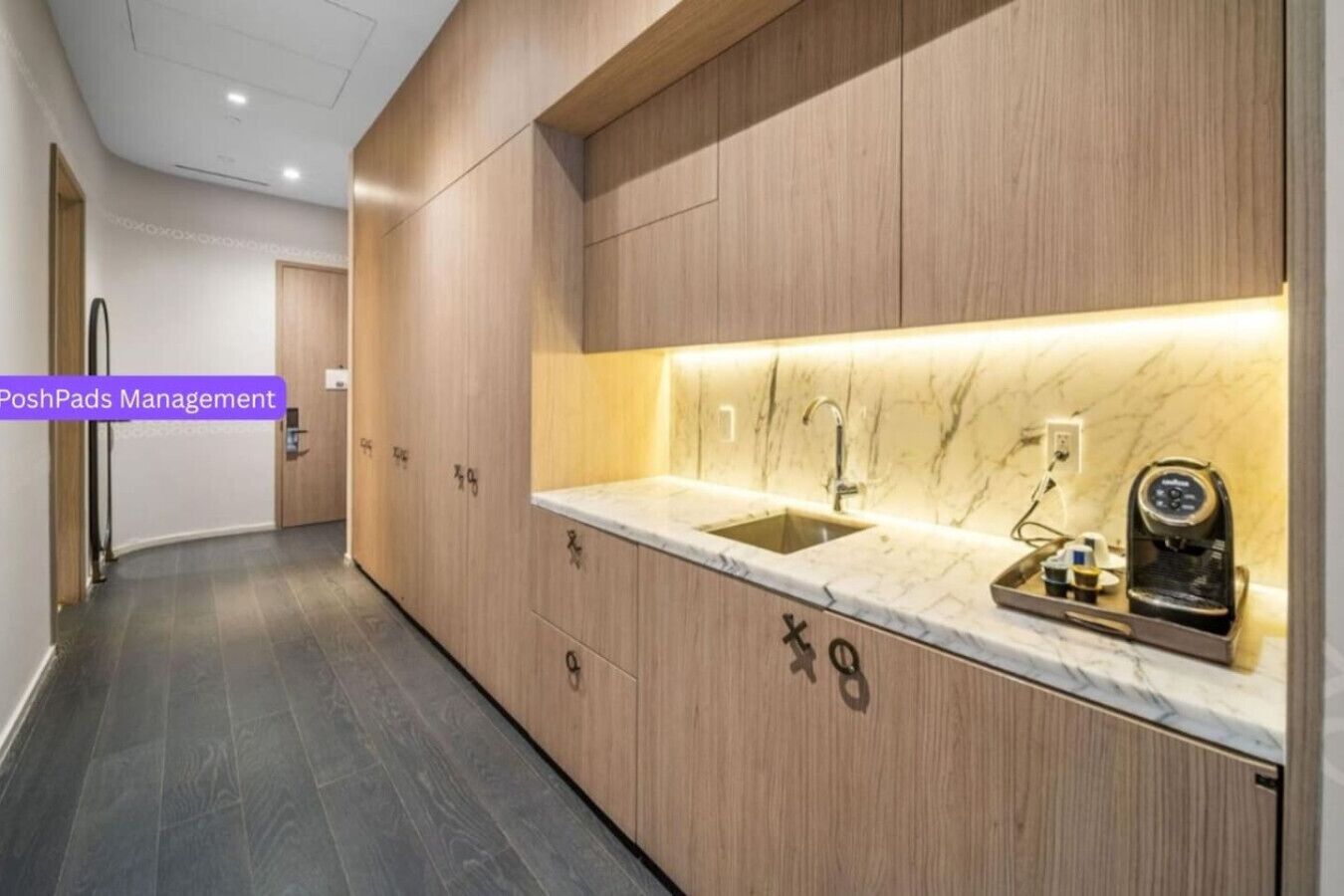 A modern kitchen with wooden cabinetry, a marble countertop, and a built-in coffee machine.